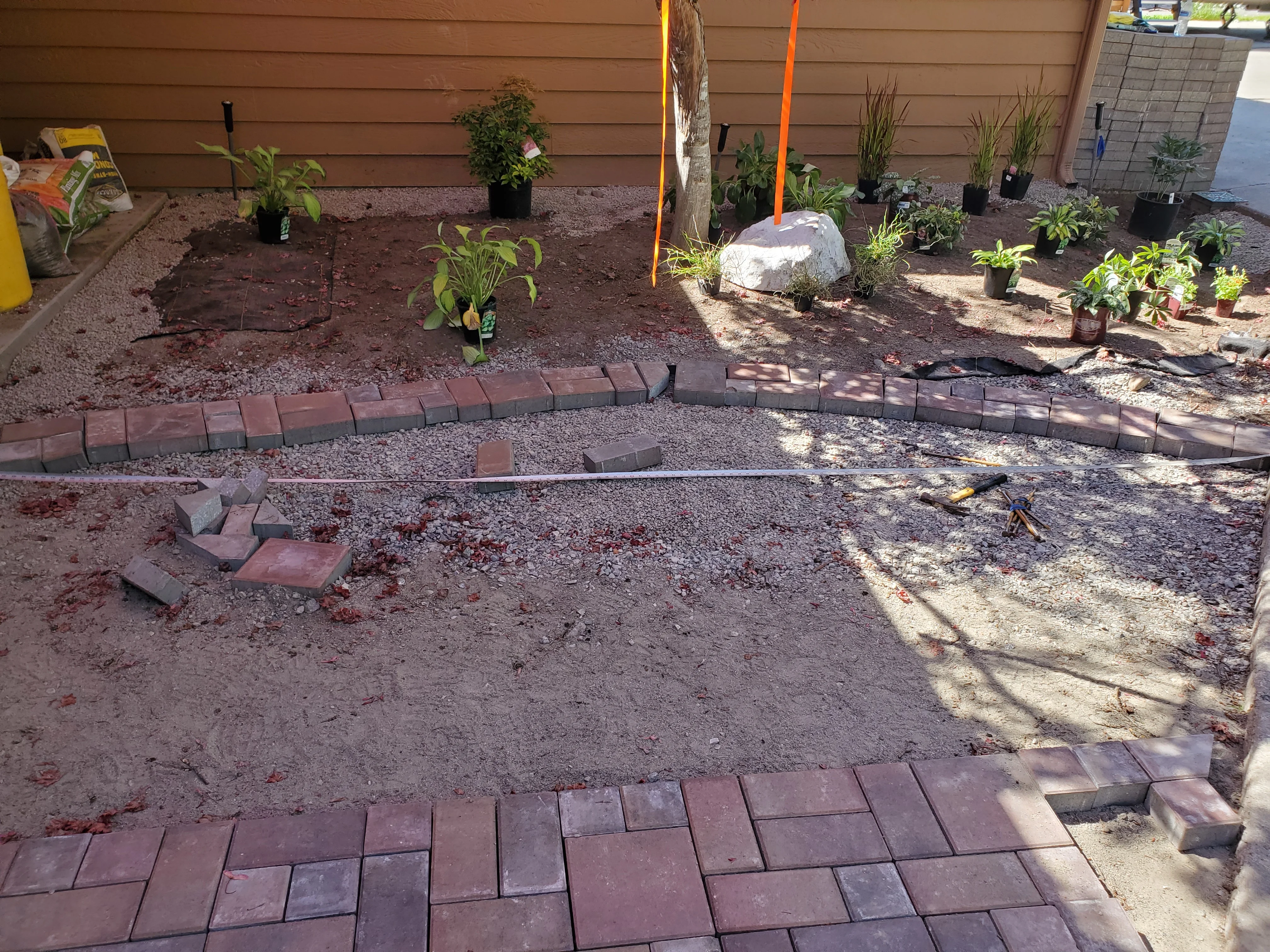 In-progress backyard hardscape with brick pavers, gravel, and newly planted landscaping beds