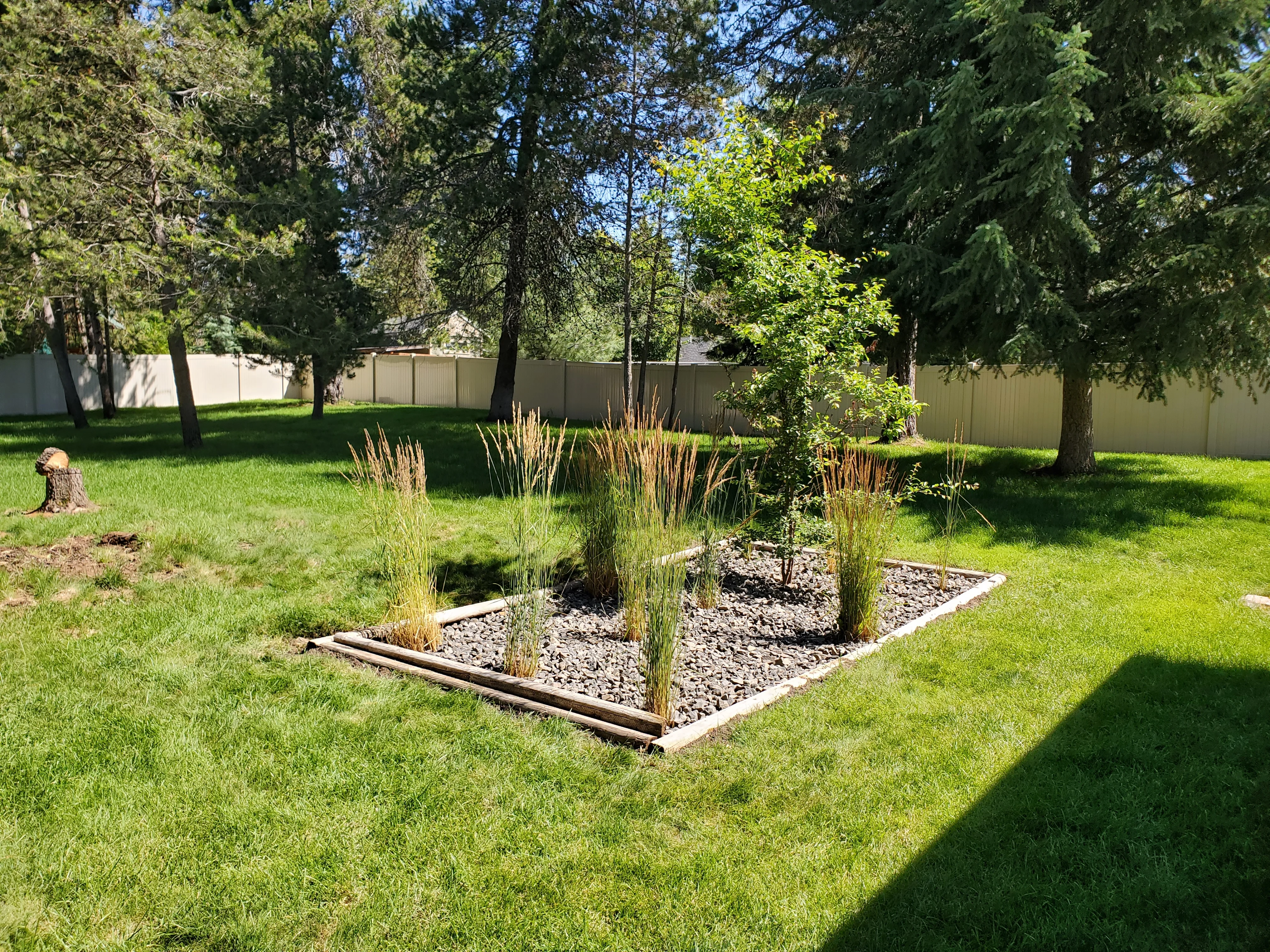 Ornamental grass planting bed with river rock mulch and timber border in residential yard