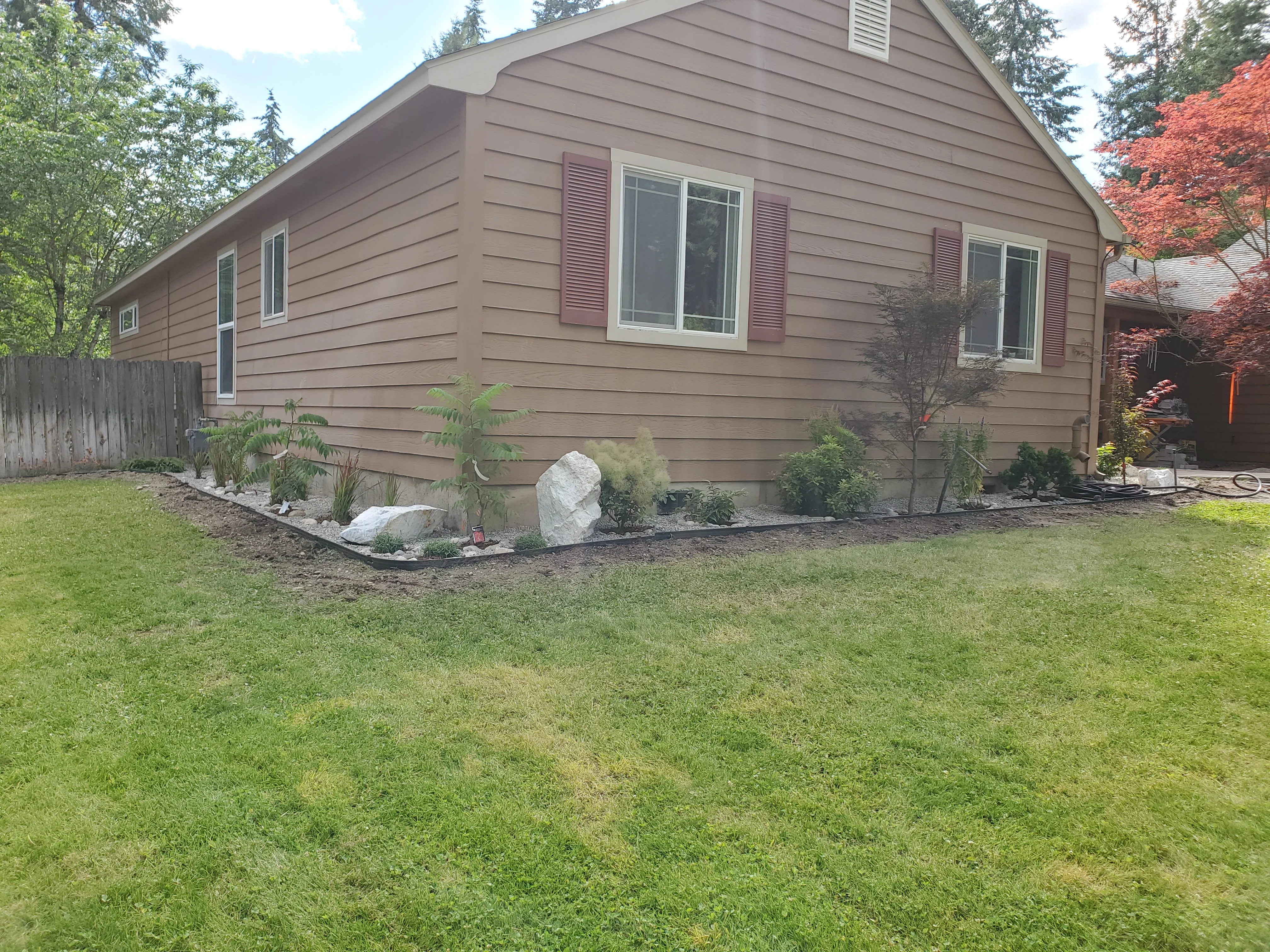 Foundation landscaping with boulders, ornamental plants, and mulch bed along house exterior