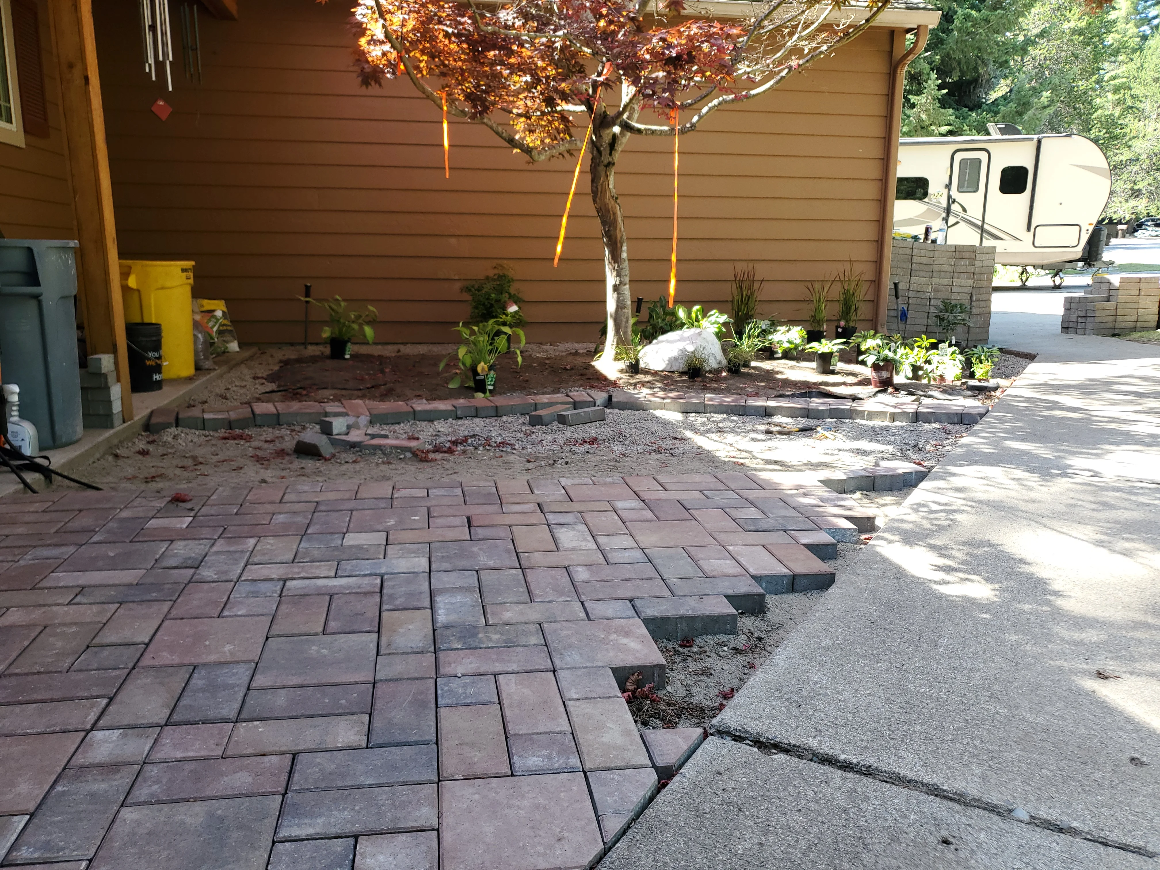 New paver patio with landscape beds and stone edging against brown siding