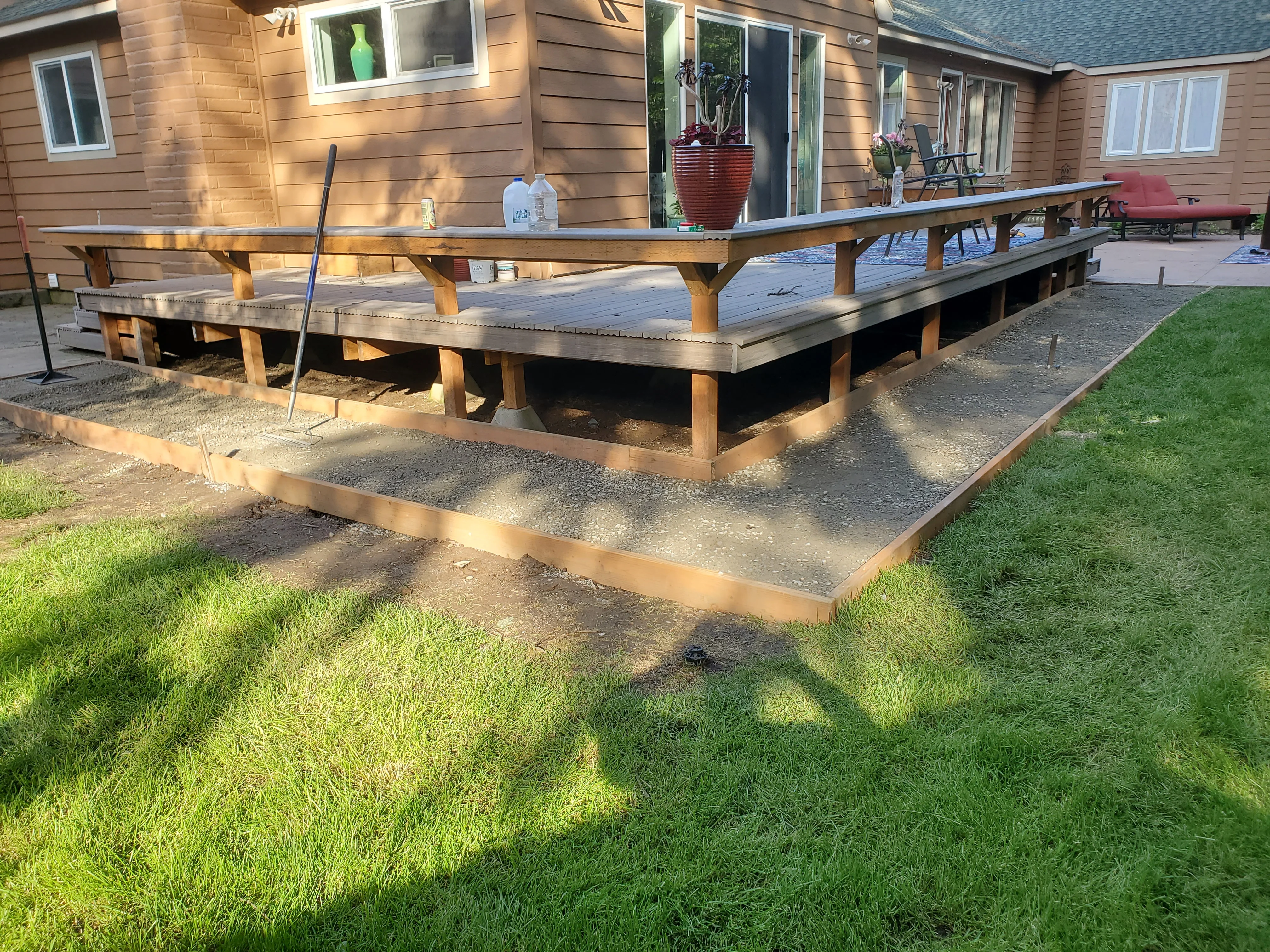 Composite deck with wooden posts and metal edging on gravel base near residential home