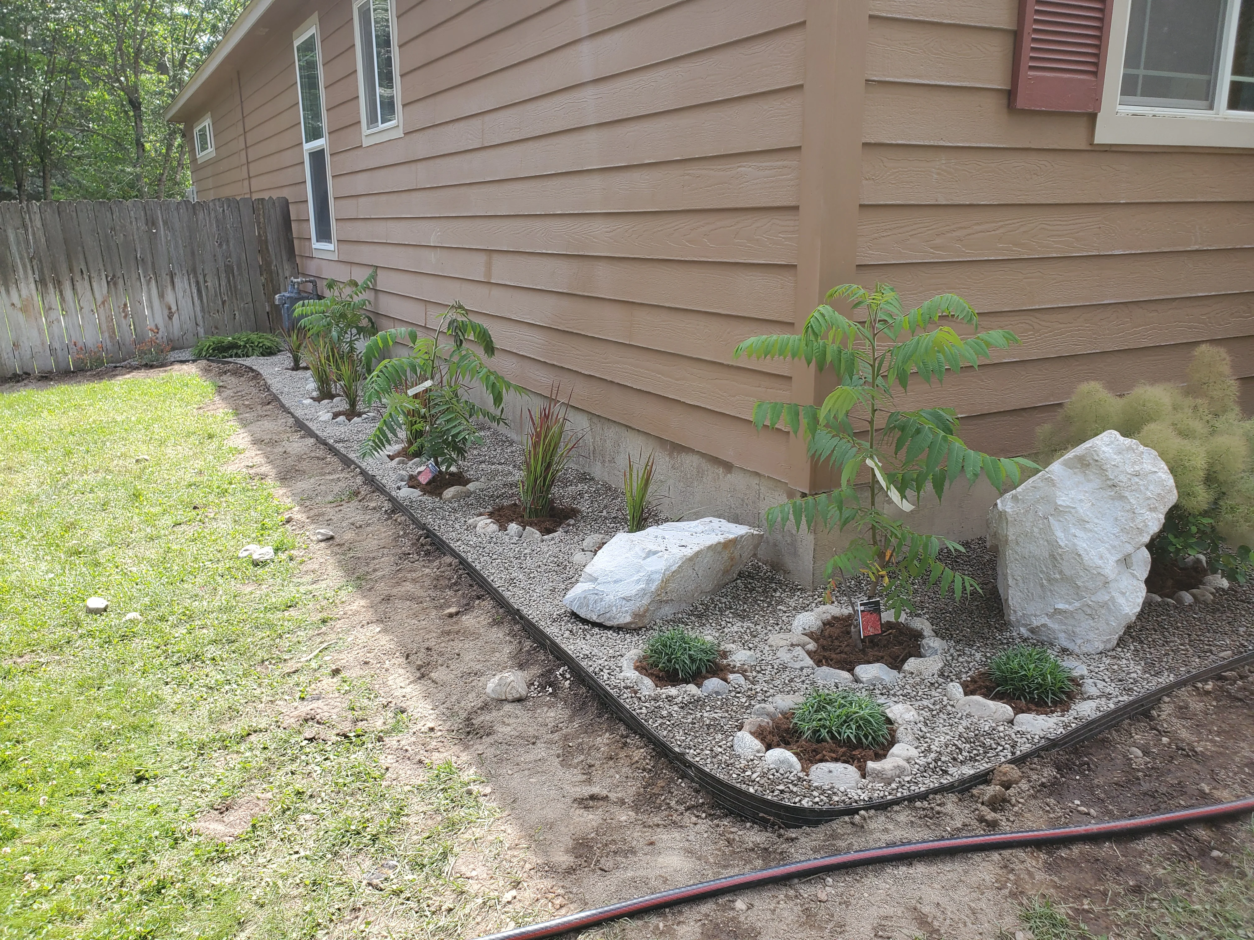 Foundation landscape bed with river rock, plants, boulders, and edging along home exterior