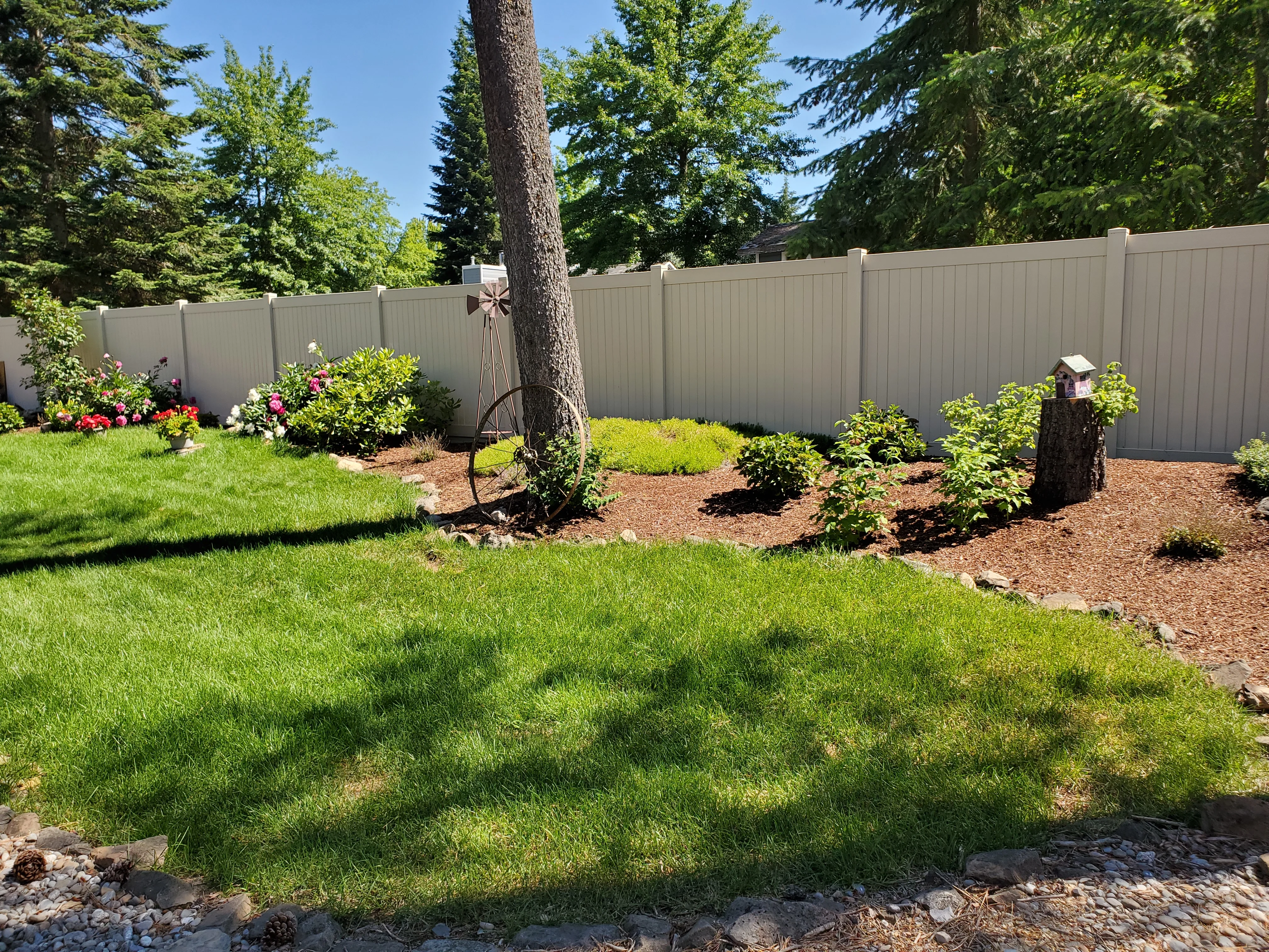 Landscaped backyard with mulch beds, flowering perennials, shrubs, and maintained lawn