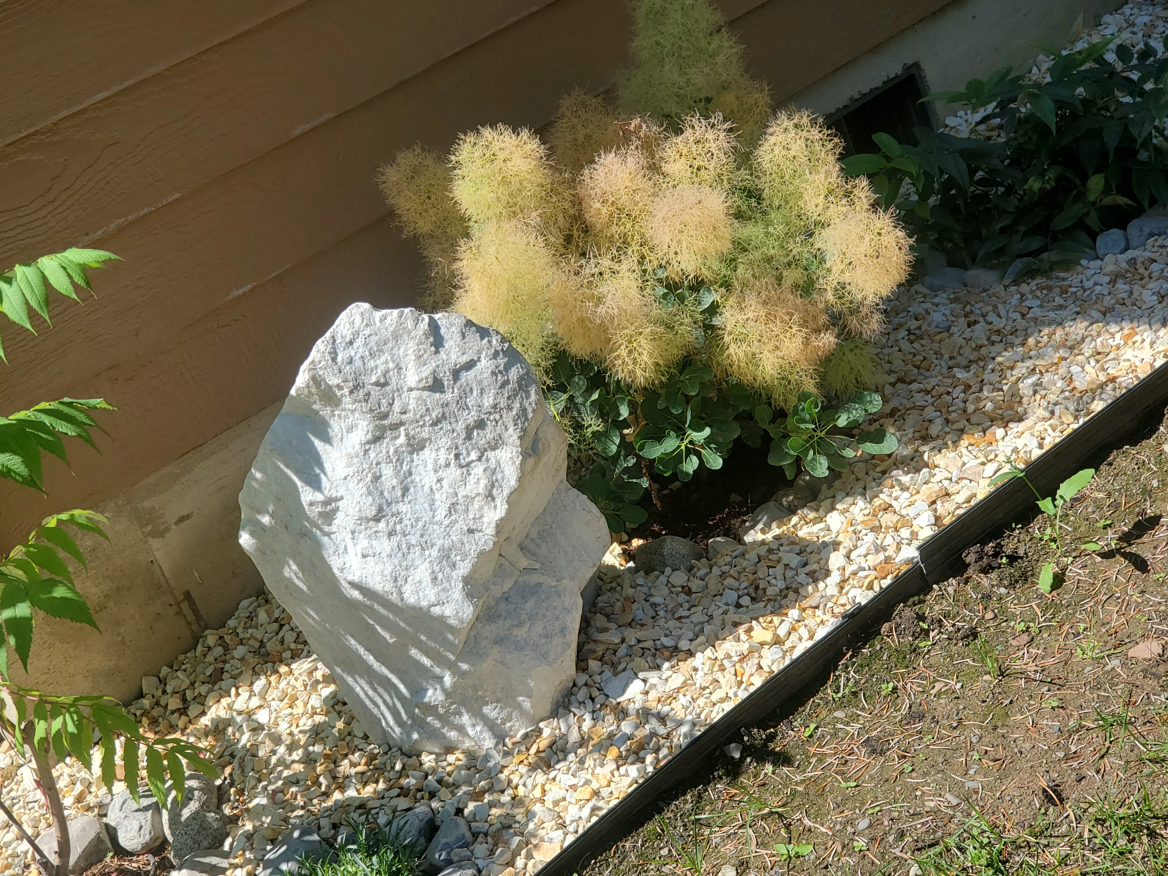 White stone feature in gravel landscape bed with ornamental grasses and shrubs