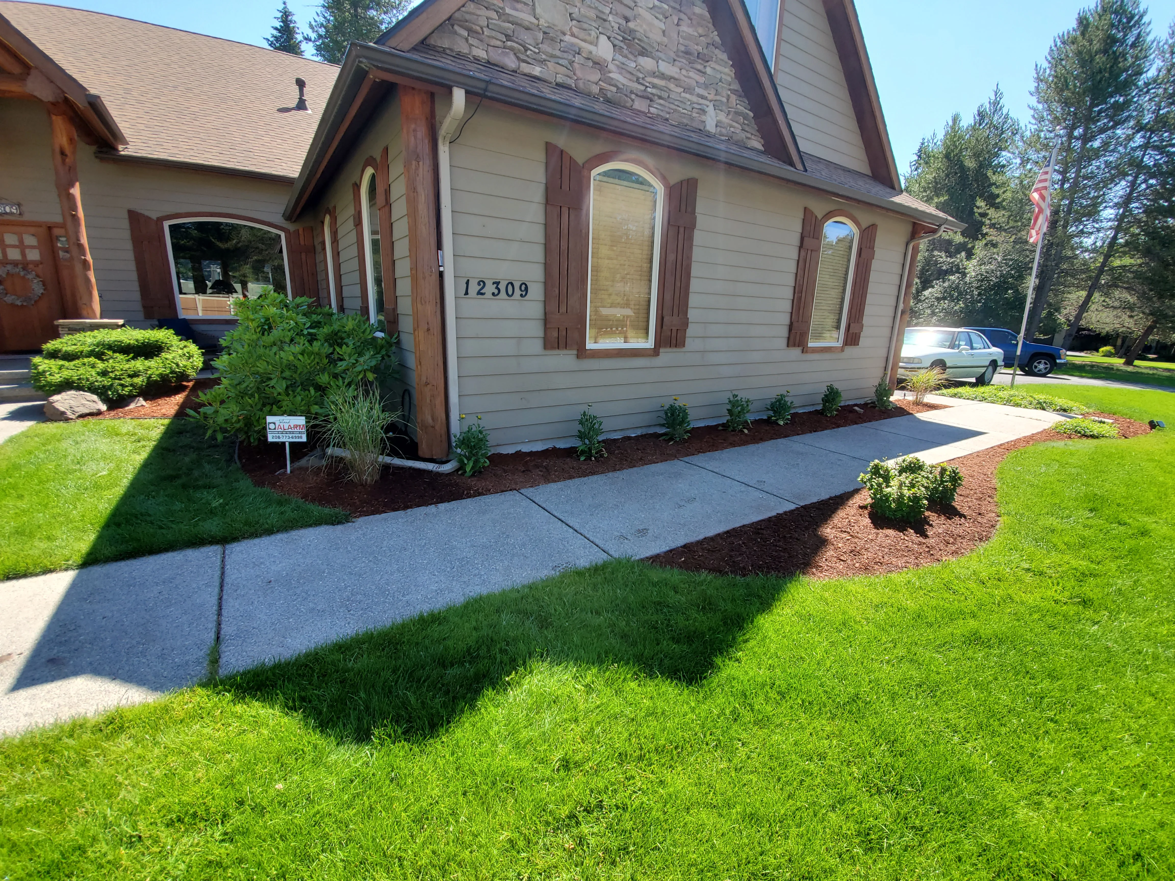Freshly installed artificial grass covering a residential backyard in Coeur d'Alene, Idaho, with clean turf edges bordered against a wood fence. The surface is flat, green, and free of bare spots, showing the finished result of a full hardscape turf installation by Bee Stung Yard Care LLC.