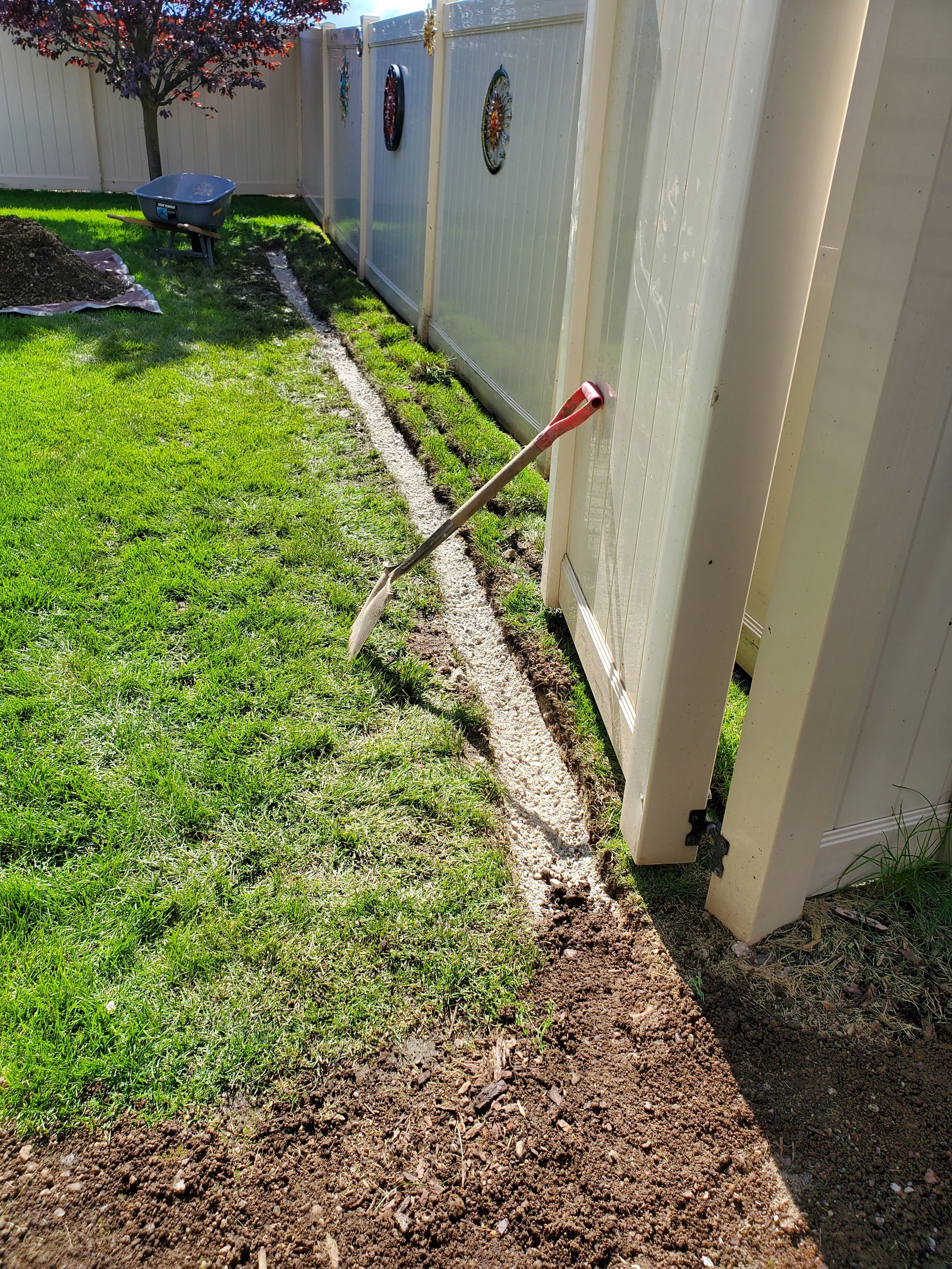 A Bee Stung Yard Care LLC technician applying granular fertilizer to a green residential lawn in Coeur d'Alene, Idaho. The yard shows even turf coverage with a backdrop of North Idaho trees and a clear blue sky.