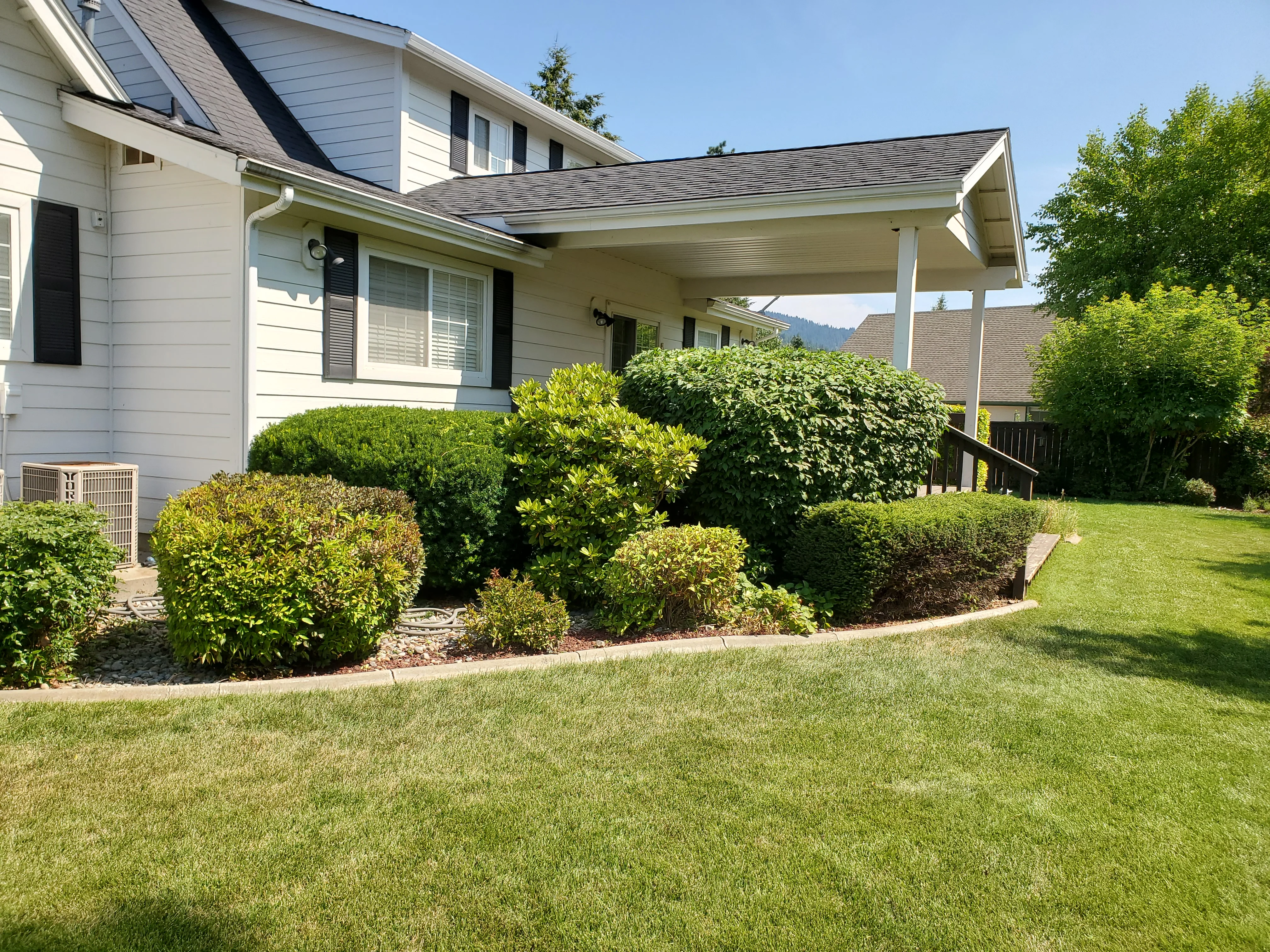 A freshly mowed residential lawn in Coeur d'Alene, Idaho with clean mowing lines, trimmed edges along a concrete driveway, and no clippings left on the sidewalk. The yard shows even grass height across a slightly sloped North Idaho property.