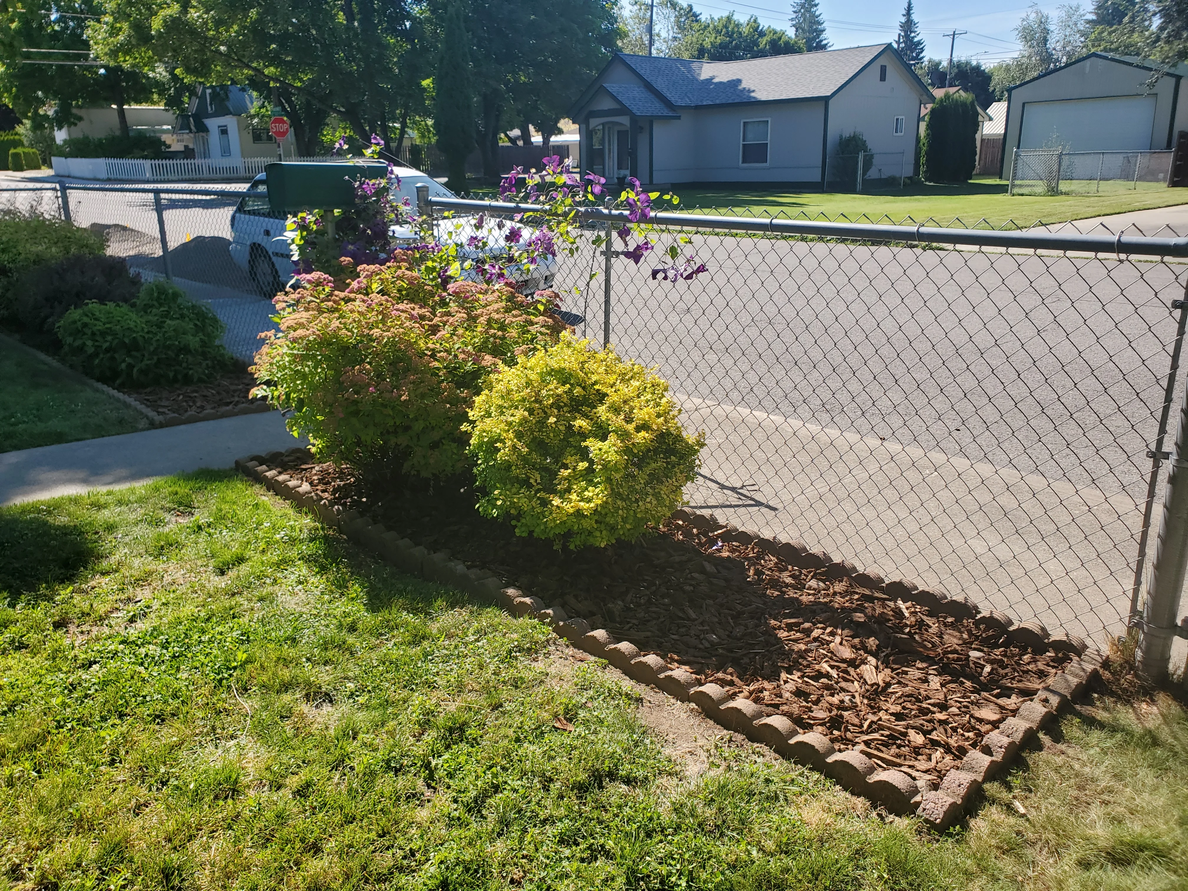 Freshly installed dark mulch covering a residential landscape bed in Coeur d'Alene, Idaho, with clean edges around shrubs and a well-defined border along a lawn. A North Idaho home exterior is visible in the background.