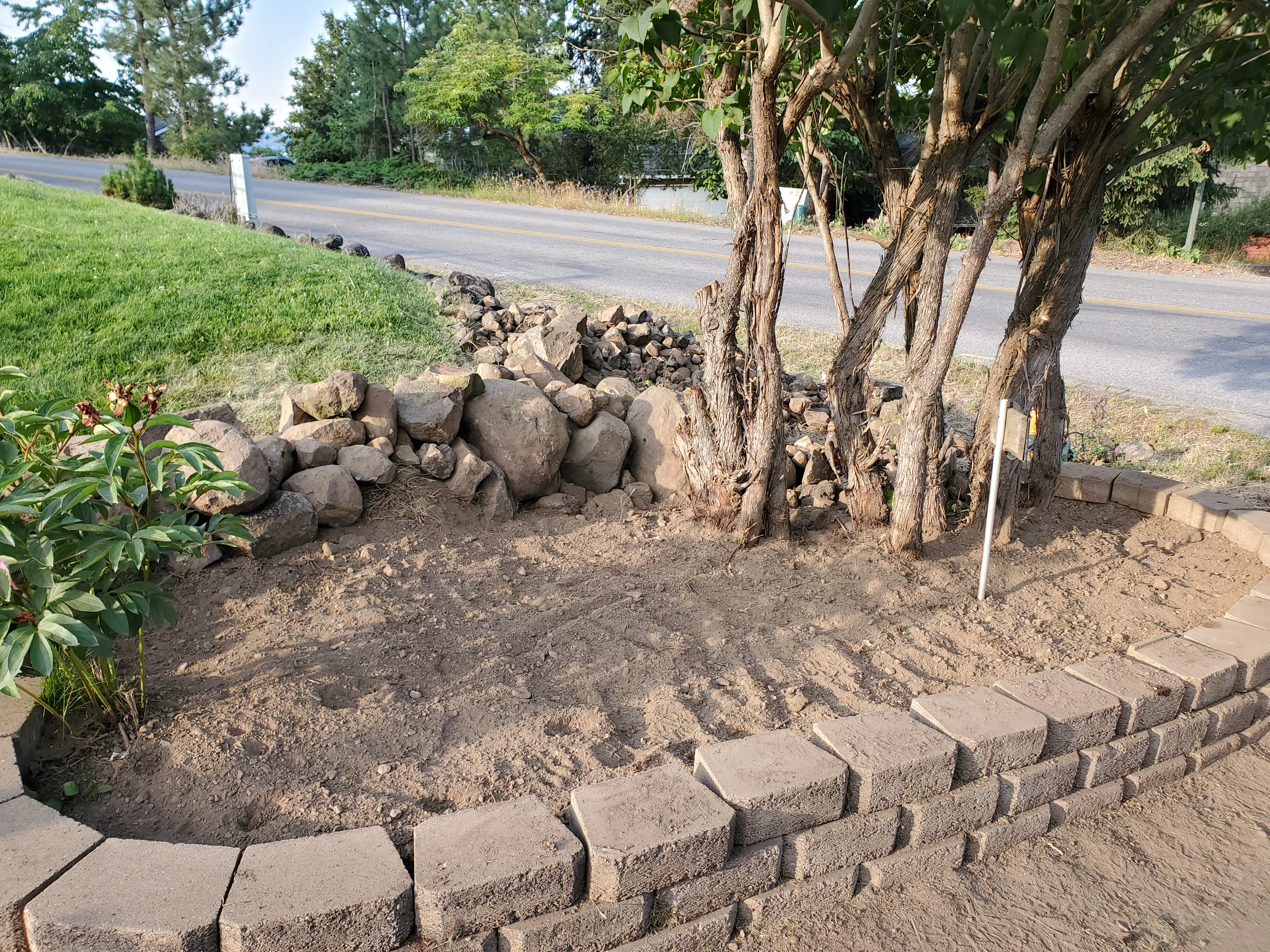 A freshly installed retaining wall on a sloped residential property in Coeur d'Alene, Idaho, with compacted base visible and level yard space created above the wall. The wall runs along the edge of a backyard with North Idaho pine trees visible in the background.