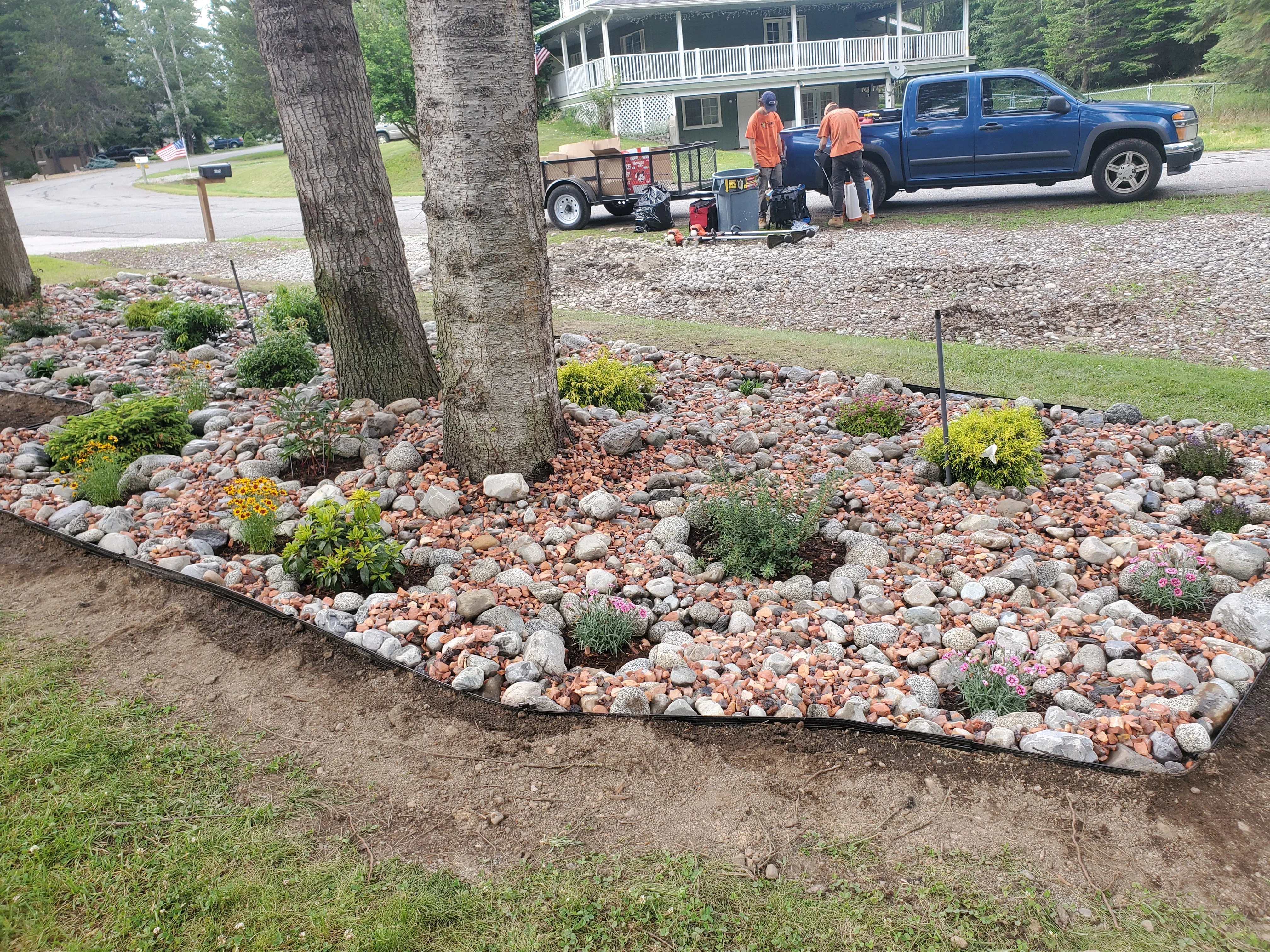 A finished rock landscaping installation at a residential property in Coeur d'Alene, Idaho, showing clean gravel beds with a weed barrier edge along a home foundation. Decorative rock covers a sloped front yard area with defined borders and no turf.